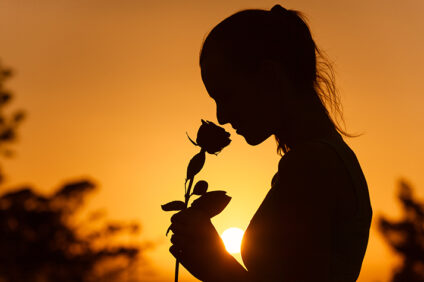 silhouette of a woman smelling a rose against a sunset