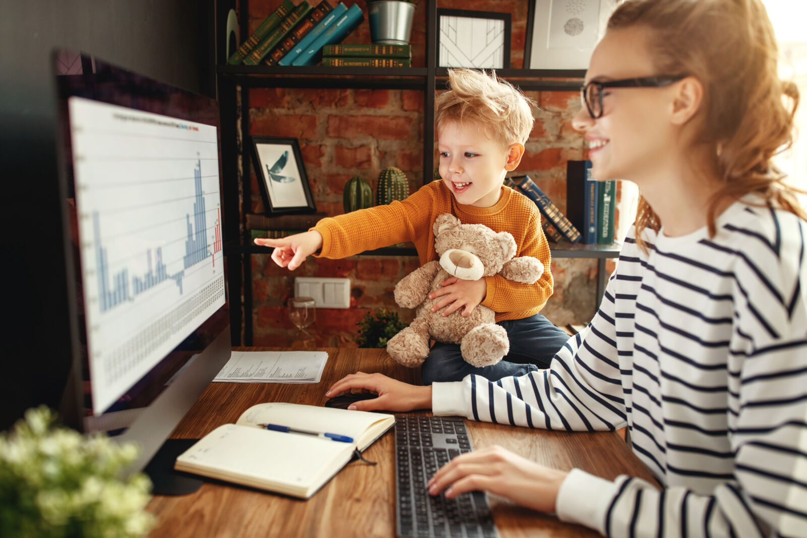 child with stuffed animal pointing at woman's computer screen