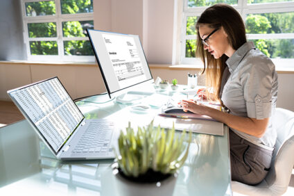 woman working on calculator in front of two computer monitors