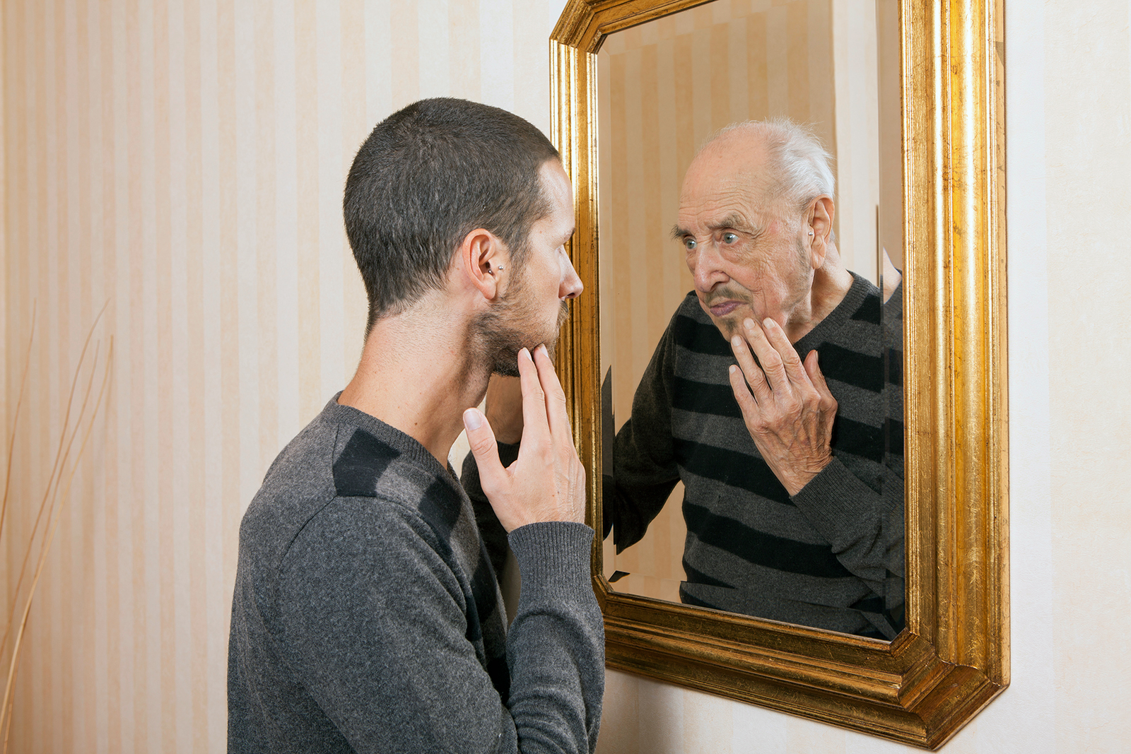 young man looks in mirror, sees older version reflected back