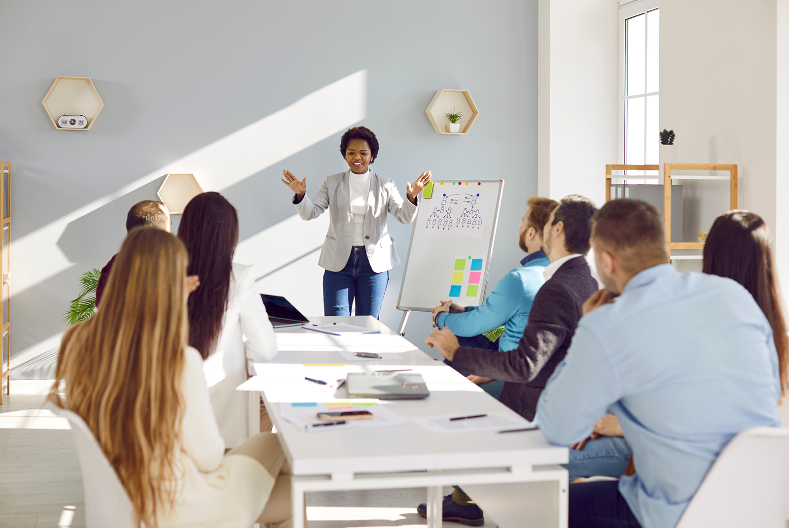 woman giving presentation to seven people with whiteboard and sticky notes