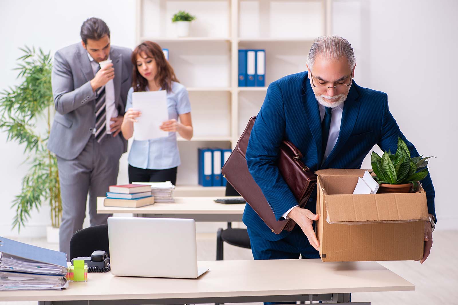 man placing box on desk to move into new job, with to coworkers in background