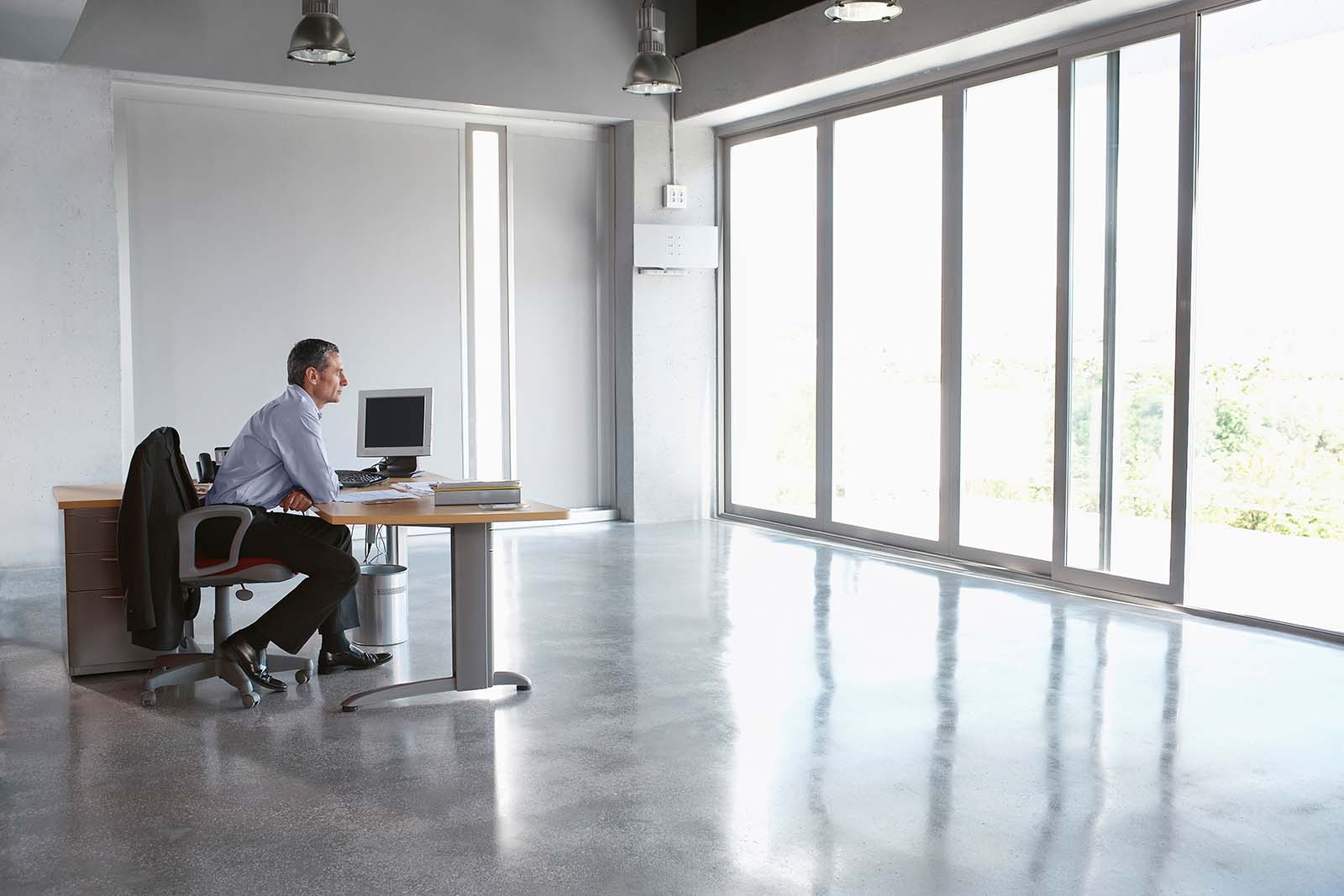 man sitting at desk in otherwise empty office, facing glass wall