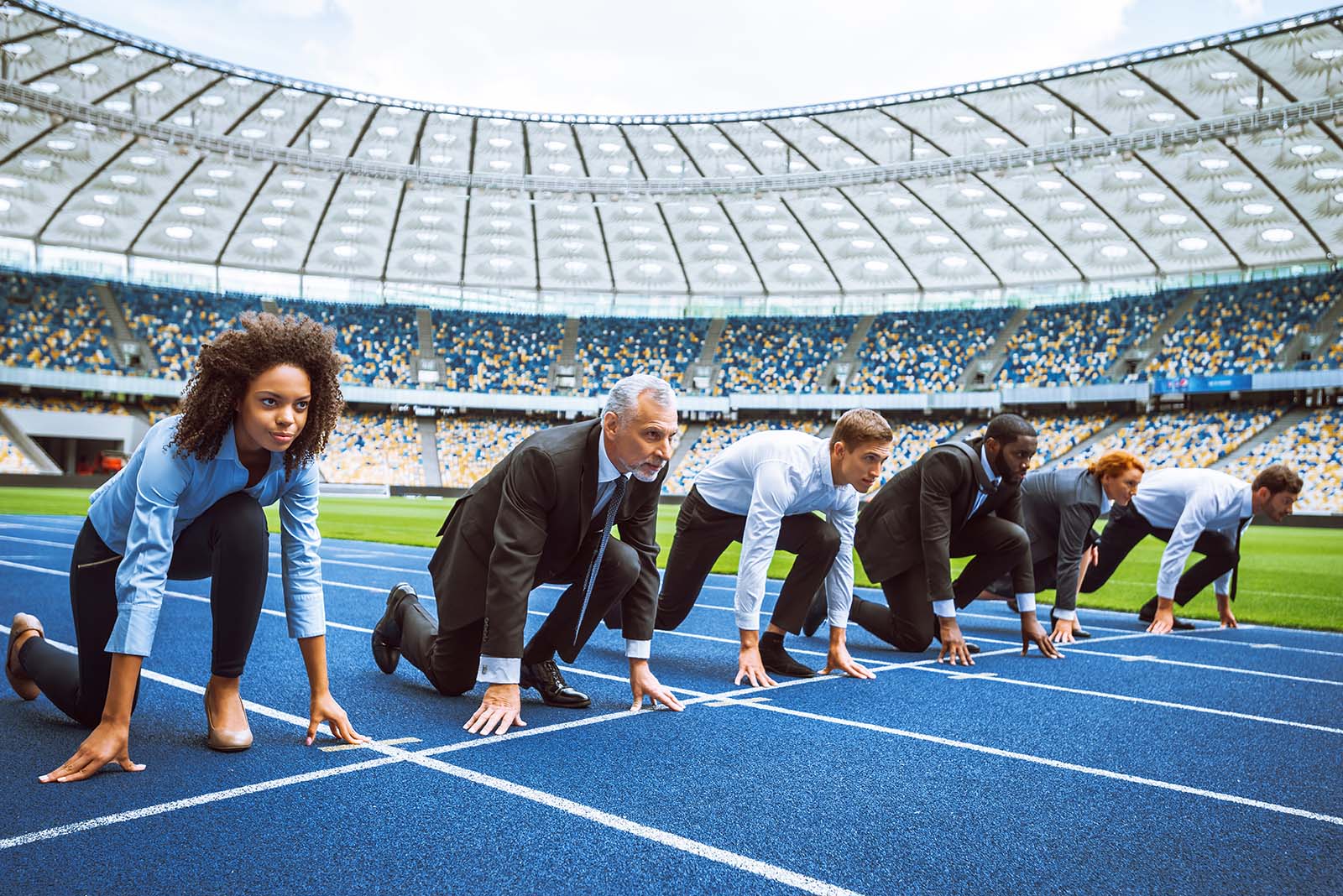 six people in business clothing lined up at start of athletic track