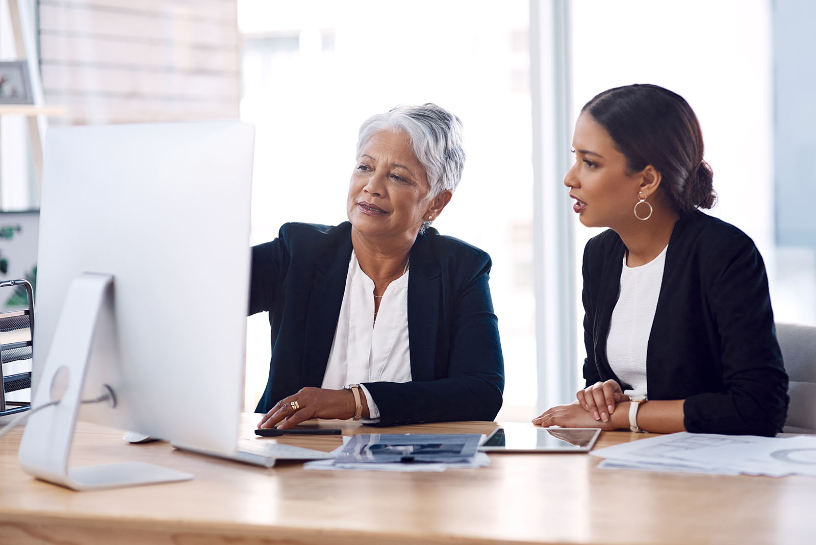 older woman showing young woman something on office computer screen