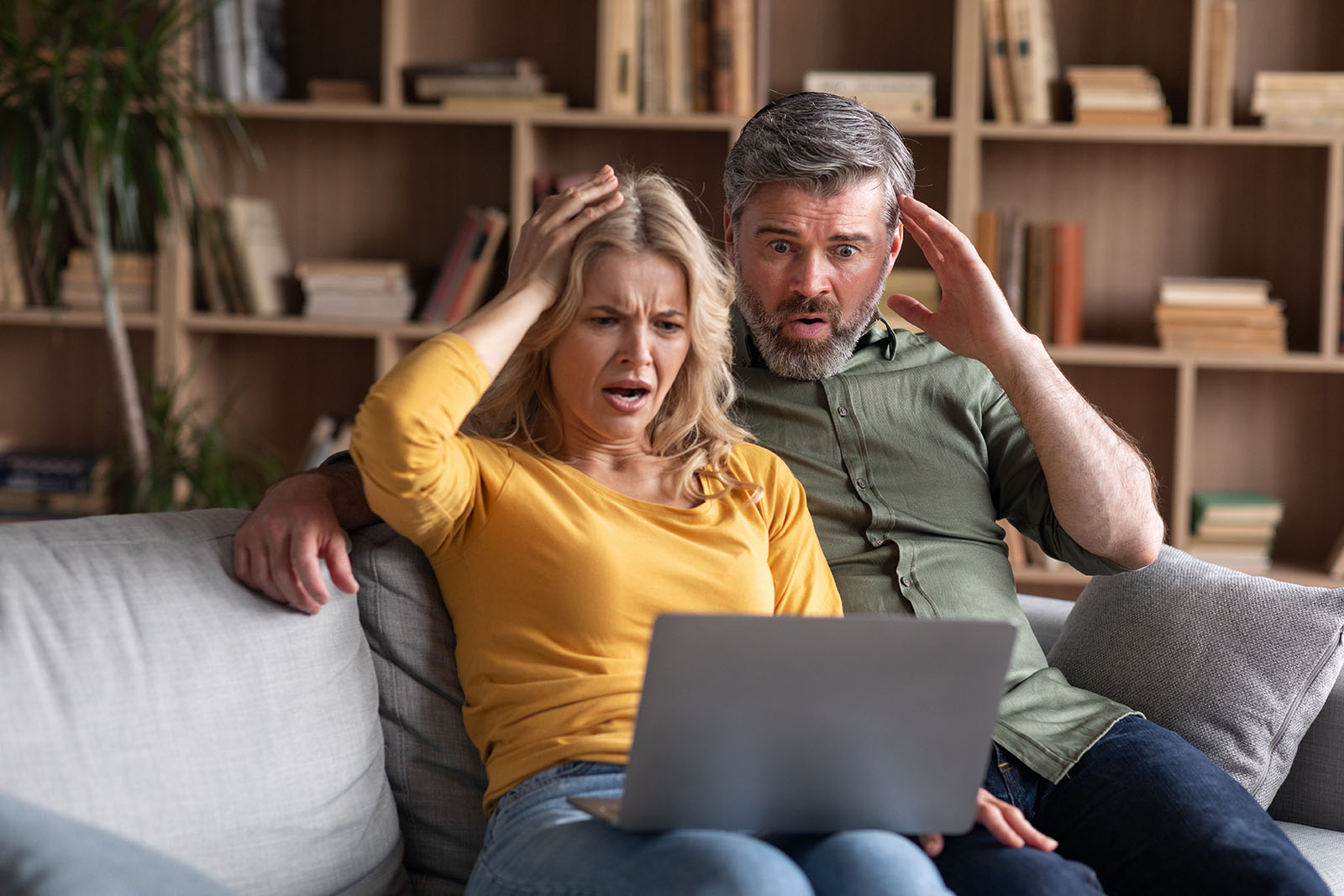 shocked couple looking at laptop while sitting on couch