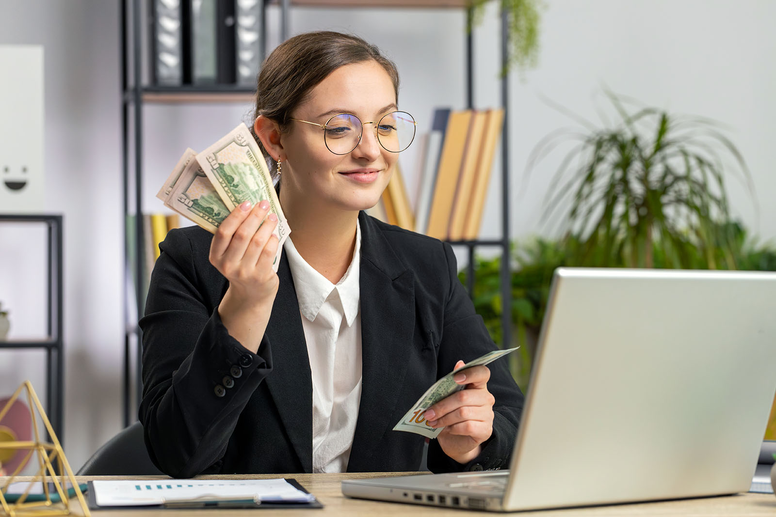young woman seated at laptop counting money