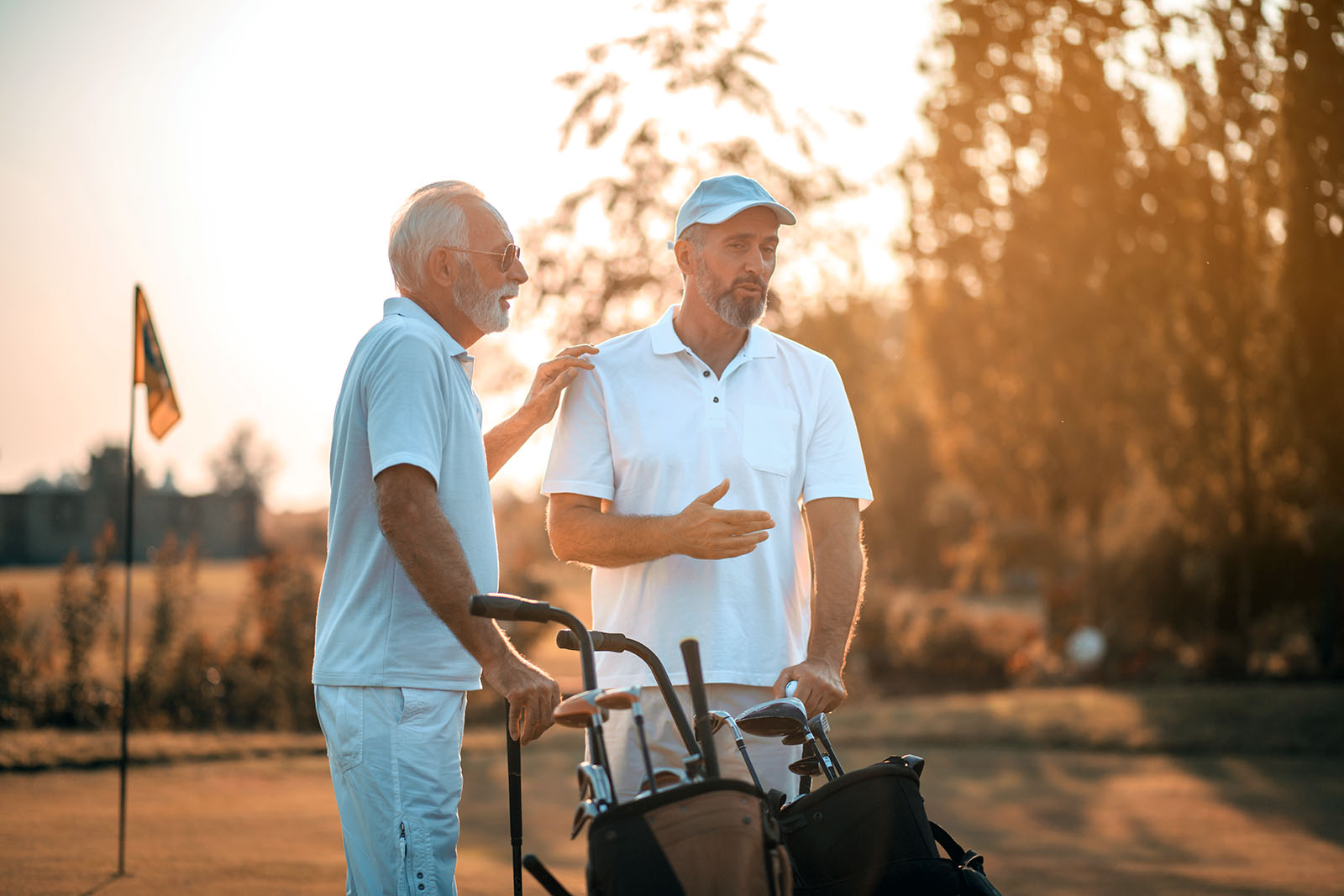 two older men pausing on golf course to talk, one has hand on other's shoulder