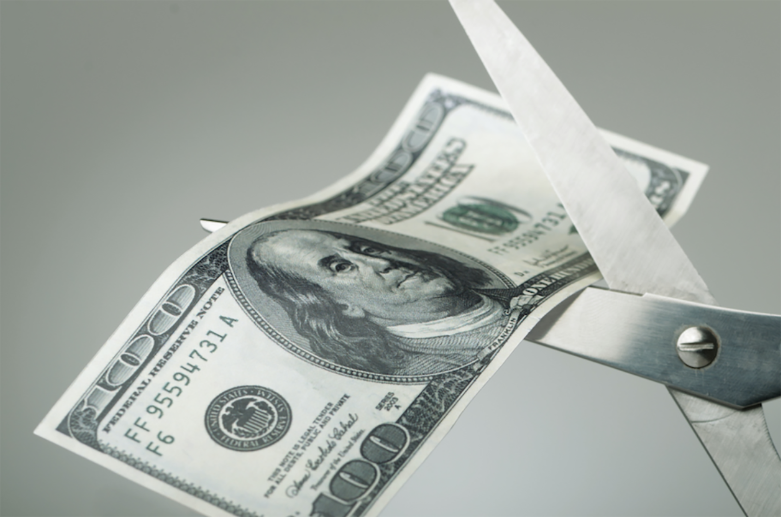 scissors cutting $100 bill in half