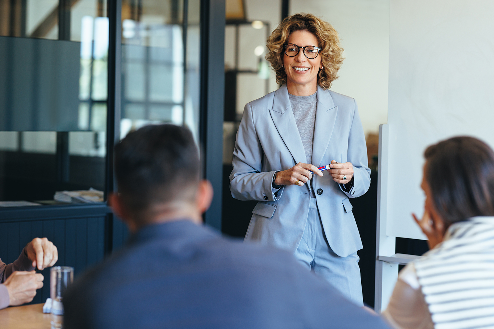 woman holding marker beside whiteboard, facing three colleagues