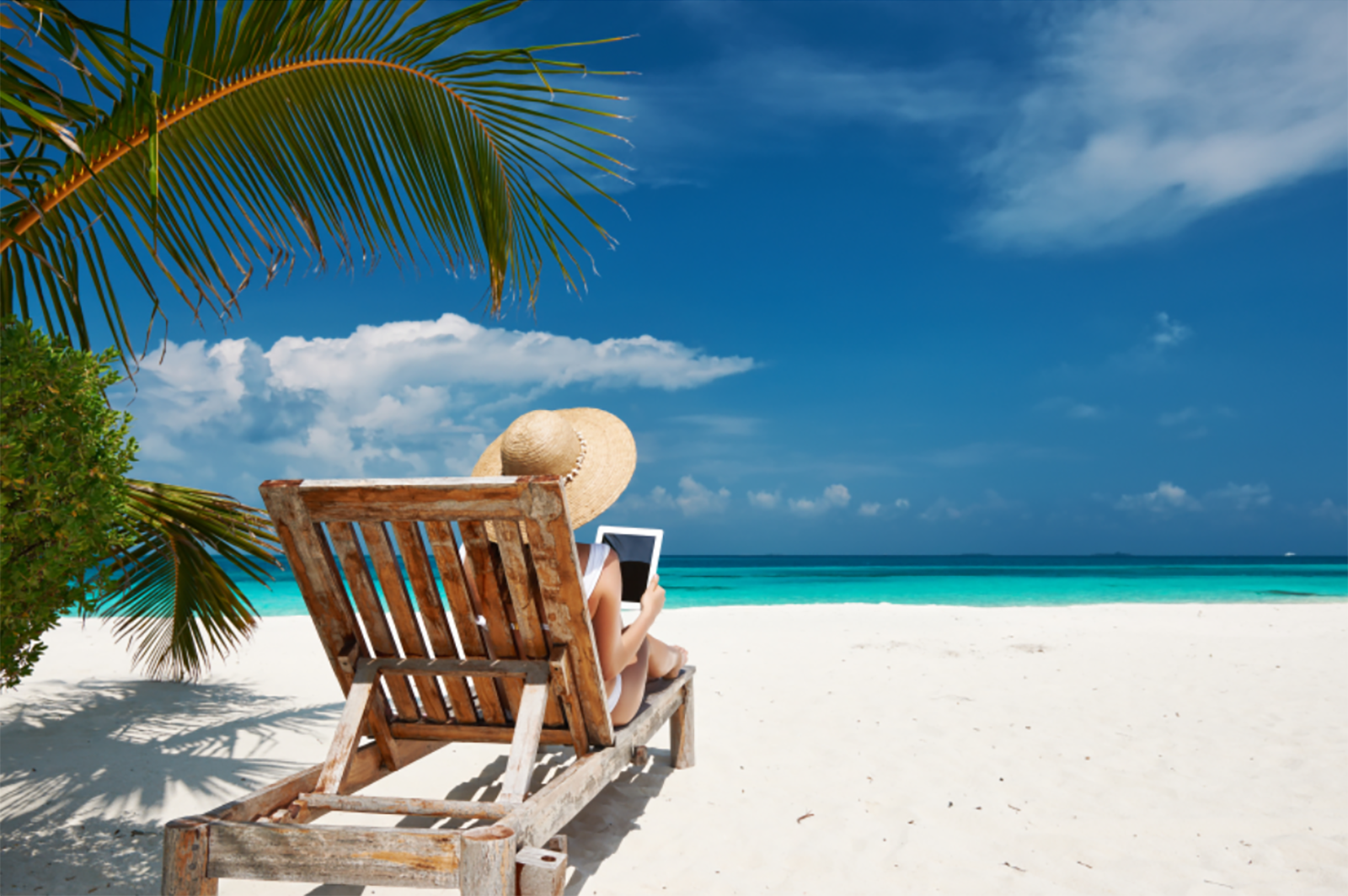 woman with tablet wearing swimsuit sitting in beach lounge chair staring out at ocean
