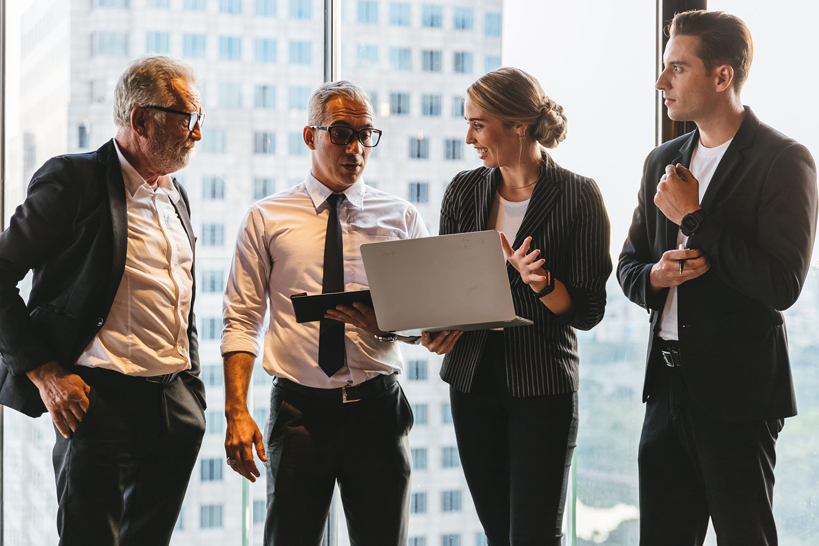 four people standing in office building and talking, two of them holding tablets