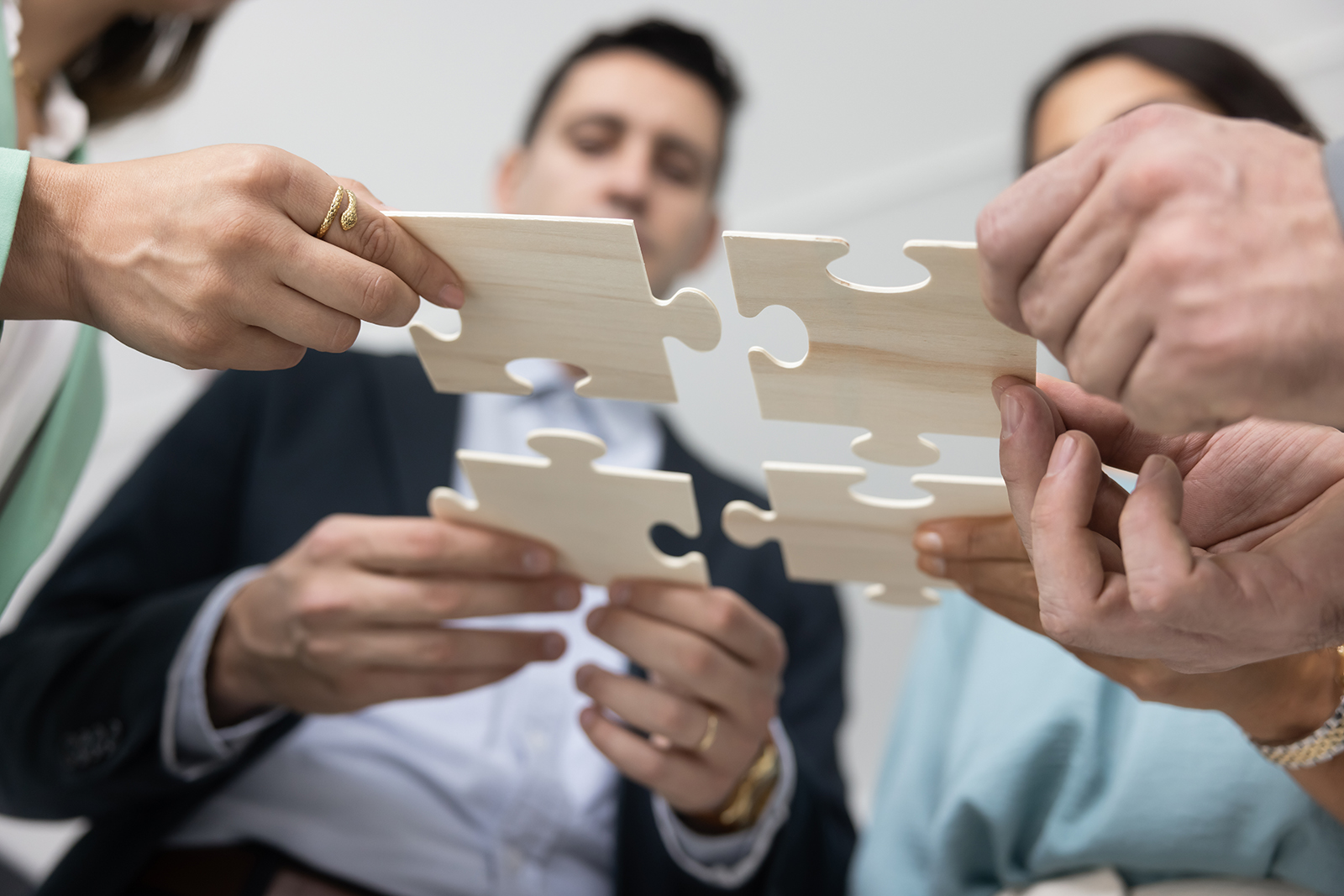 view from below of four people, each holding a jigsaw puzzle piece and matching it to the others