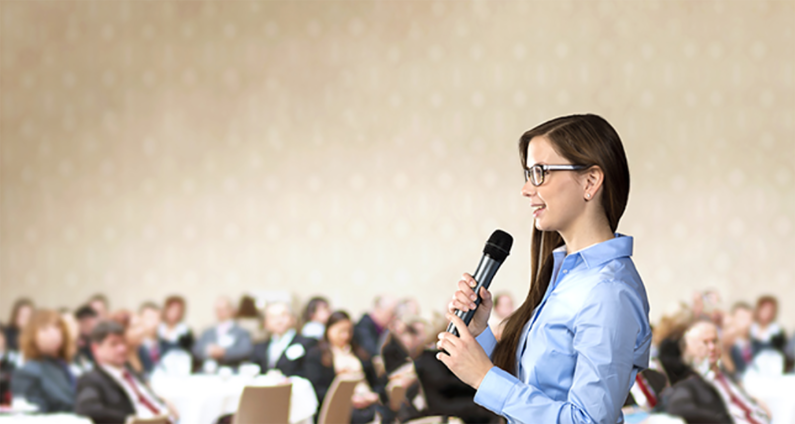 woman speaking to handheld microphone in room full of people