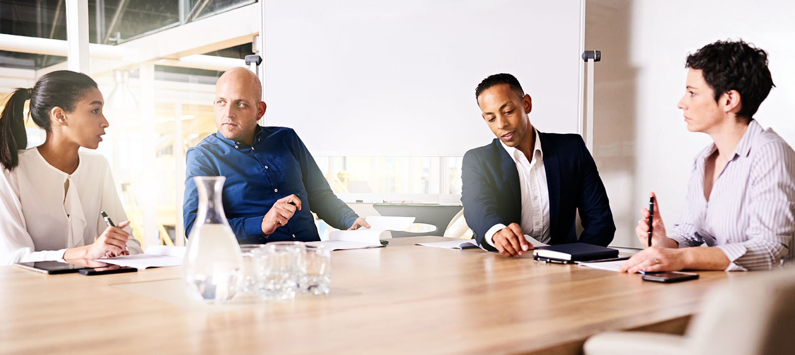 four businesspeople seated around table with whiteboard behind them